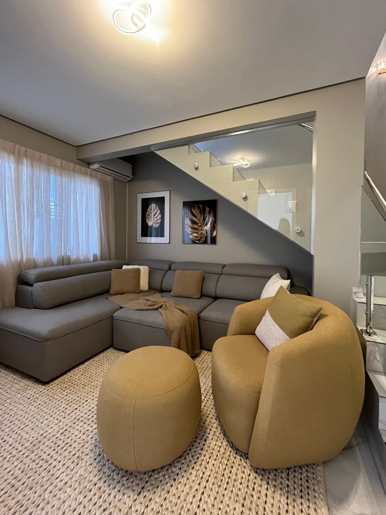 Sala de estar clara com sofá cinza, poltronas curvas e tapete, resultado de uma consultoria