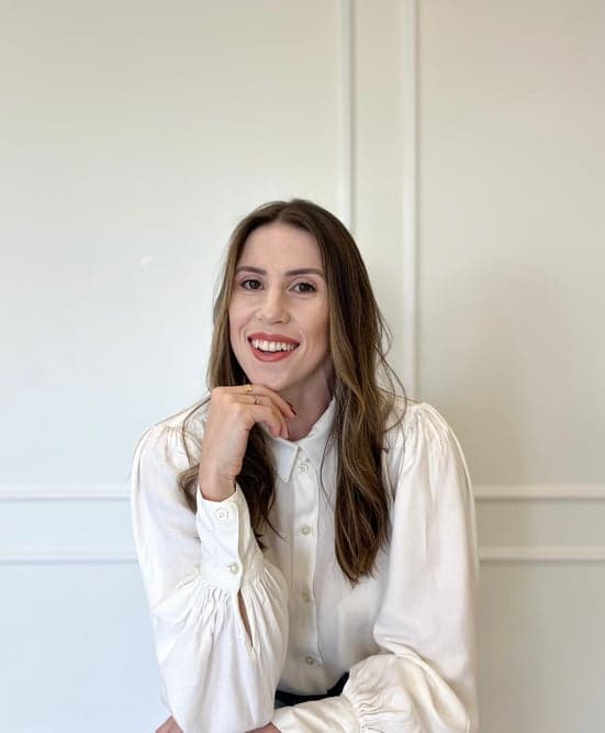 Arquiteta Mariana Coppini sorrindo, com camisa branca, em frente a uma parede com boiserie